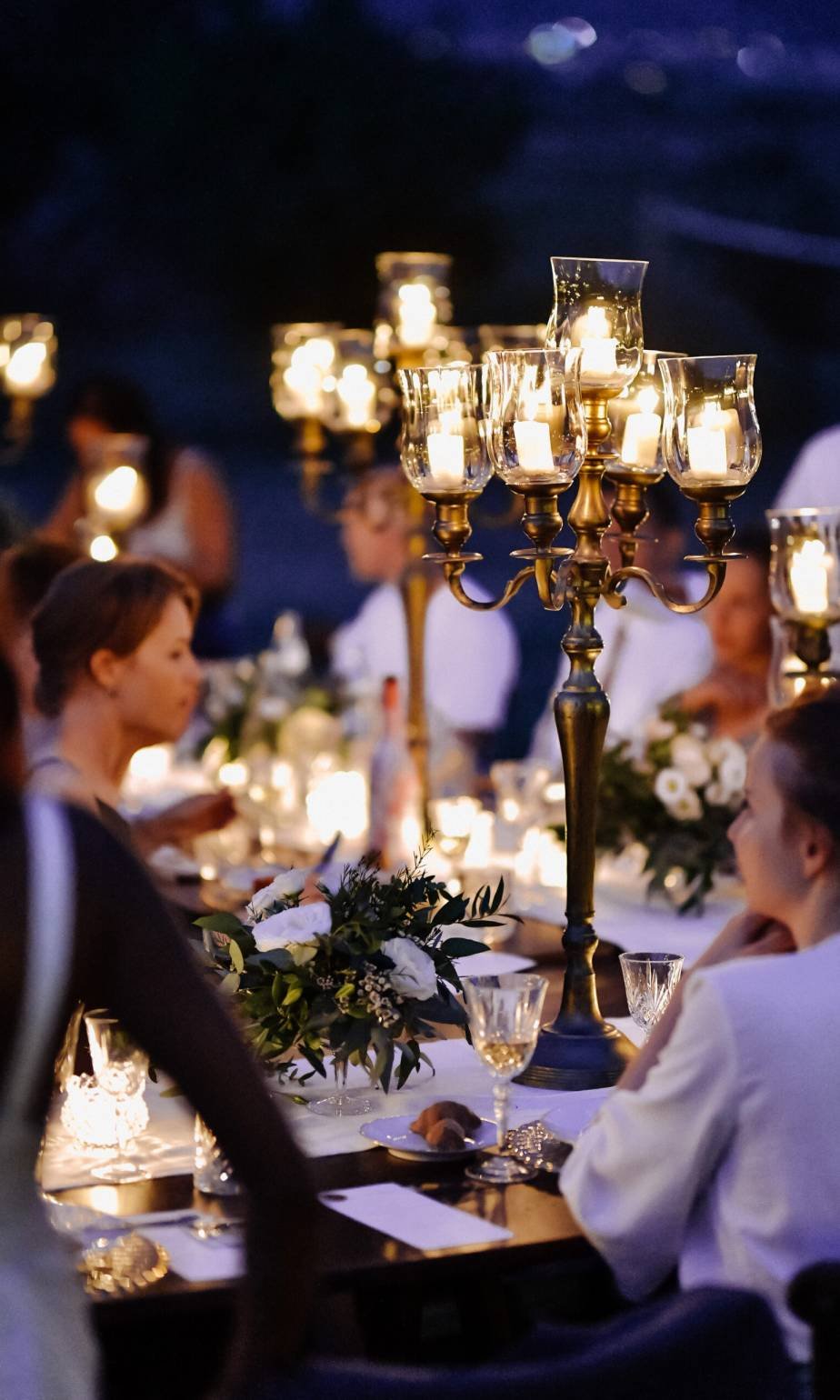 Decorated tables with floral composition and old fashioned candlesticks and guests in the celebration evening